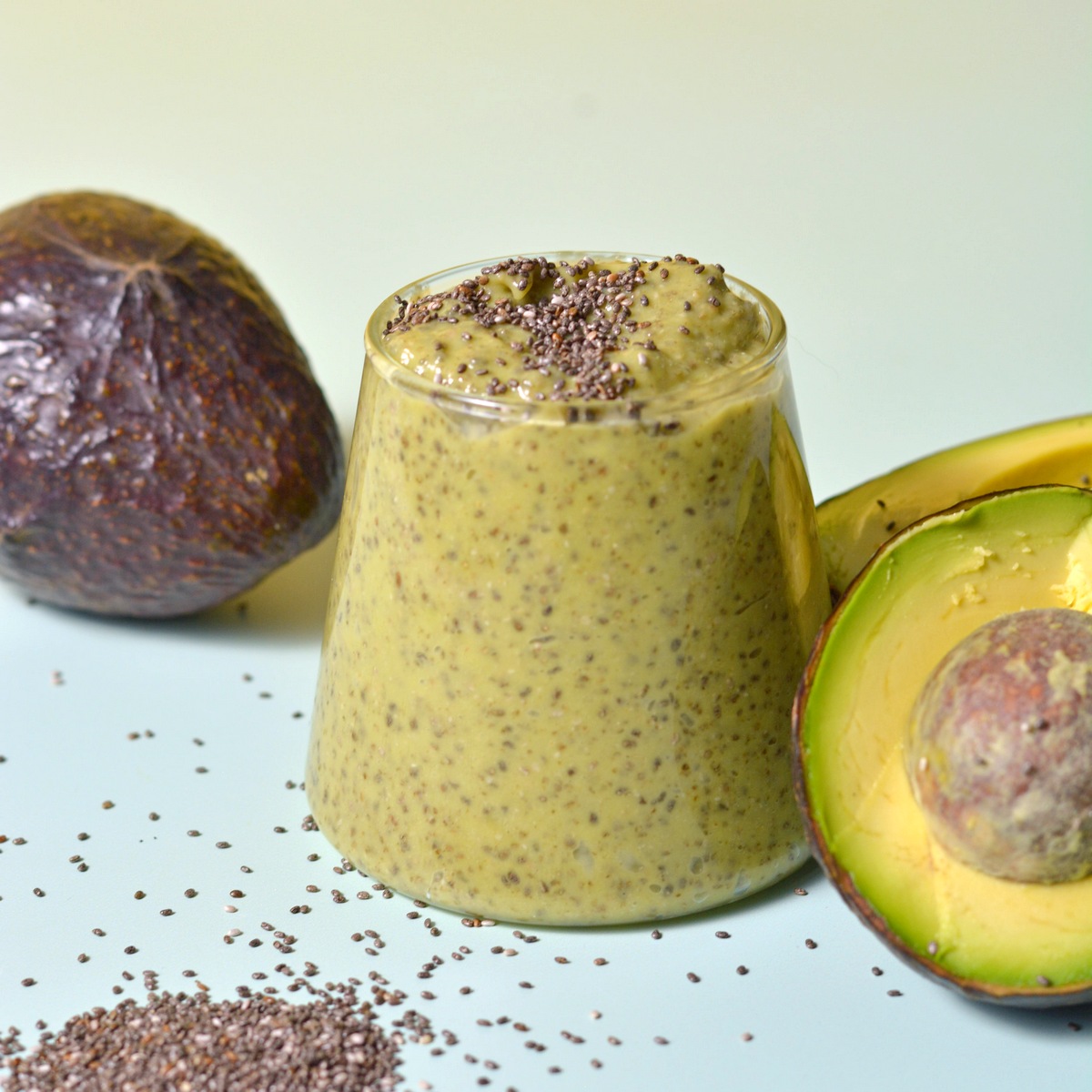 Avocado chia pudding in a glass with avocados on the side.