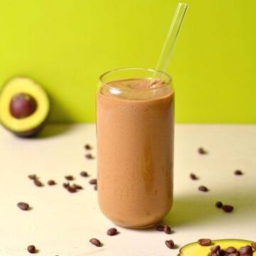A glass filled with avocado coffee with a glass straw.