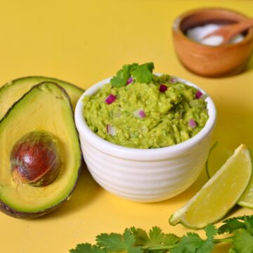 Guacamole in a white bowl with ingredients around it.