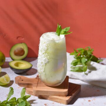 Avocado limeade on coasters in front of a red background.