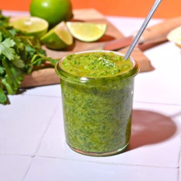 Avocado sauce in a jar in front of an orange background.