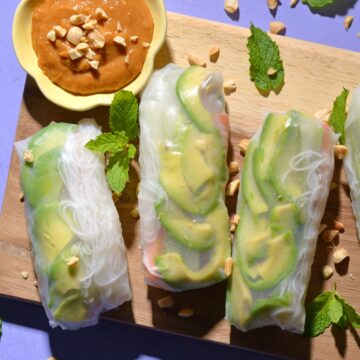 Spring rolls on a wood board next to peanut ginger dipping sauce.